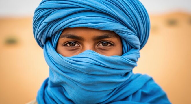 Portrait of a young Tuareg boy, blue tagelmust and traditional face veil, curious and proud gaze, Sahara Desert, North Africa