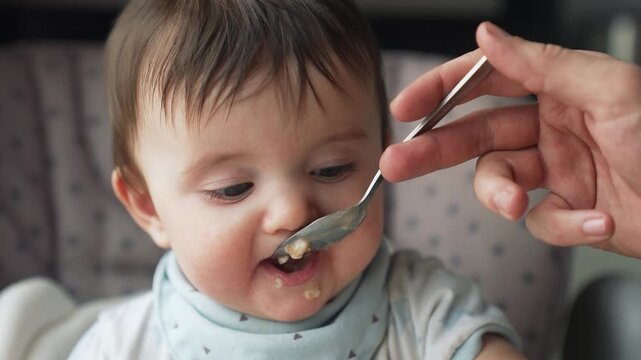Adorable baby with messy face eating meal in highchair. Infant learning to eat solid foods with porridge on chin and mouth. Toddler enjoying mealtime, developing feeding skills during weaning.