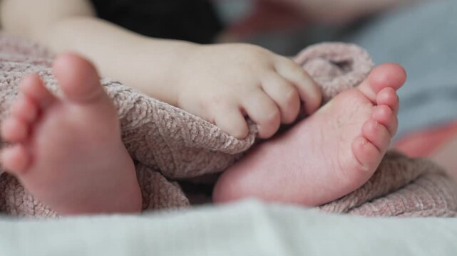 Baby feet and hands resting on soft knitted blanket closeup. Infant toes wrapped in cozy textile. Newborn child sleeping peacefully. Tiny baby fingers on warm fabric. Infant foot detail.