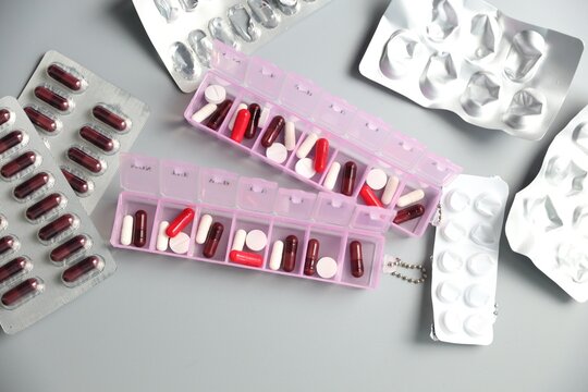 Pill organizers with medications and empty blisters on light grey background, flat lay