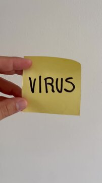 Hand holding sticky note with word Virus written in black marker