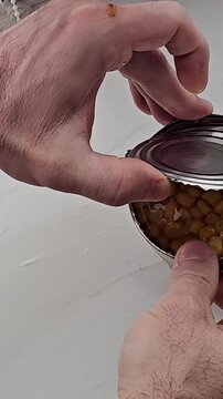 Hands opening tin can with corn kernels, close-up. Showing how to open a can with pull tab. Corns canned goods non-perishable food storage products in the home kitchen.