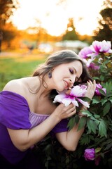 Naklejka premium Woman hugs flowers in a park during daytime while wearing a purple dress and enjoying nature