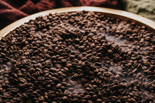 Granos de caf&eacute; reci&eacute;n tostados sobre charola dorada.