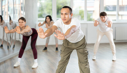 Fototapeta premium Positive sporty Asian guy doing stretching warm-up before group training in dance class for youth