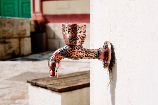 Close up of an intricately patterned copper faucet designed for ritual washing within a mosque's peaceful ablution area on a sunny day