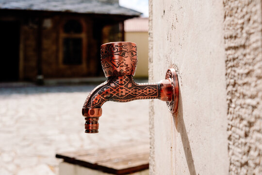 Intricate copper faucet with Islamic patterns for ritual ablutions at a sunny mosque