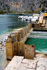Obraz premium Sheet piling creates a dry work area for harbor development on a waterfront, with boats docked nearby and a dramatic rocky landscape beyond