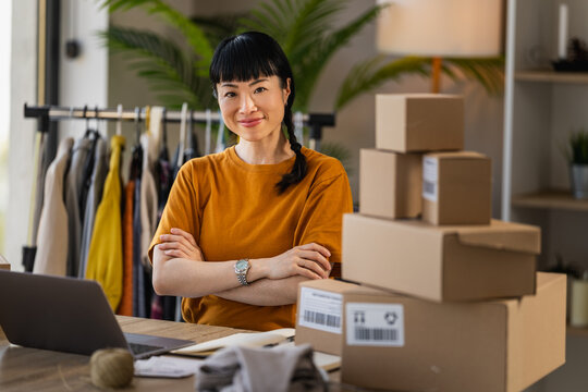 Small business owner packing orders at home office with clothing rack and laptop