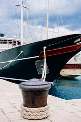 Obraz premium Textured mooring ropes loop around a sturdy bollard on the waterfront, firmly holding a sleek vessel against the calm harbor waters