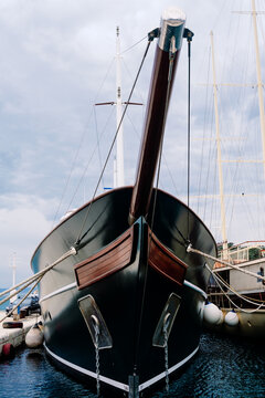 Dark yacht's elegant bow with wood bowsprit moored in tranquil marina, awaiting adventure