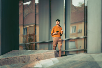Young professional woman walking outside modern office building with smartphone and coffee cup © ivanko80