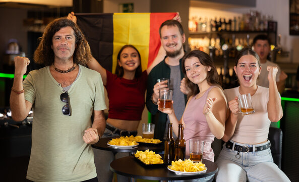 Happy girls adm men with Belgian flag celebrates the victory of her favorite team in a beer bar