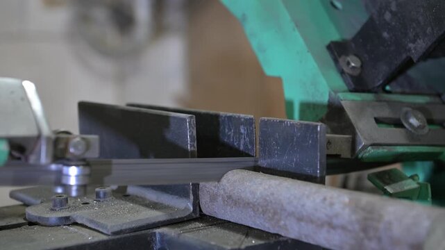 The lathe is in the production room. An electric metal cutting machine saws off a piece of metal with an automatic hacksaw to make a product
