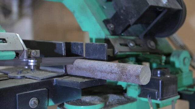 The lathe is in the production room. An electric metal cutting machine saws off a piece of metal with an automatic hacksaw to make a product