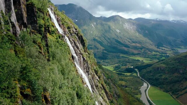 Aerial view of majestic Waterfall cascading into a wild Mountain River valley in Klakegg, Norway. Scenic epic summer wilderness landscape in Scandinavia in July. 4K establishing drone zoom in footage