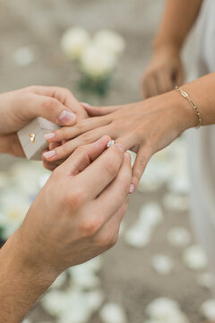Closeup of a man's hand putting on an engagement ring after his bride said yes during a proposal