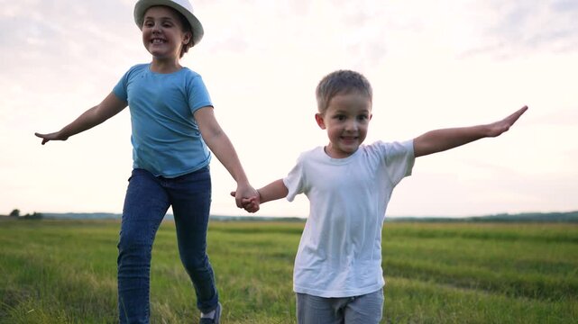 Happy children running on green field holding hands. Kids play outdoors in summer meadow. Smiling boy and girl run together. Children enjoy freedom in open field. Joyful kids in nature.