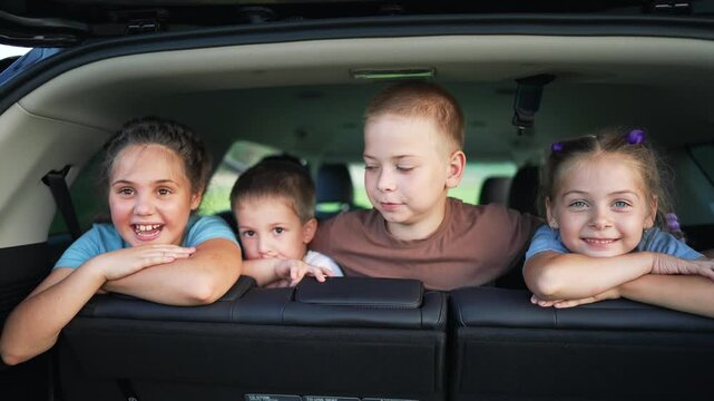 Happy children laughing in car back seat. Four kids smile and laugh together during family trip. Children lean over rear seat in SUV. Happy kids enjoy road trip. Family travel with laughing children.