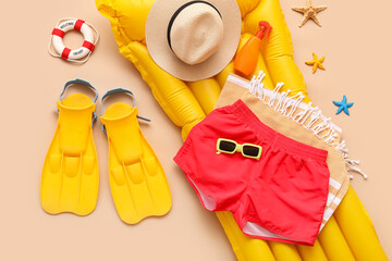 Swimming trunks with inflatable mattress and beach accessories on beige background © Pixel-Shot