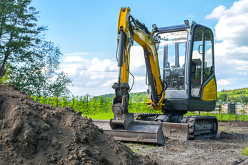 Small excavator in front of a pile of topsoil, ready to level the ground, garden and landscape...