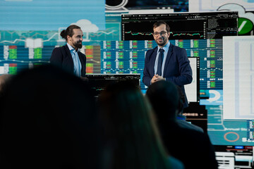 Fototapeta premium Team of CEOs making a presentation with business indicators for panel discussion on stage at international summit in auditorium. Professional men in suits hosting networking event and forum.