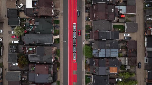Top down overhead of streetcar traveling on red painted dedicated lane through residential neighborhood with regular traffic and city homes in North America