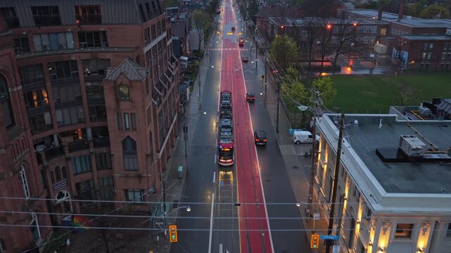 Red streetcar navigating dedicated transit lane on King Street in Toronto, evening traffic moving alongside historic buildings, lights reflecting on wet pavement