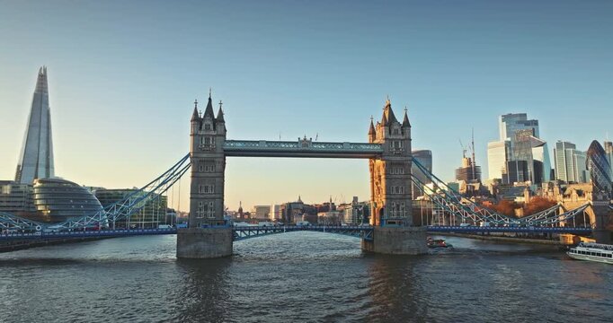 Tower Bridge and the Shard flank the City of London skyline, golden hour light reflecting on the Thames and modern glass towers rising beside historic bridges and river traffic. Drone zoom out flight