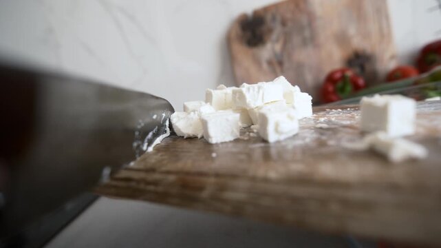 Chef Knife Drops Crumbled Feta Cheese From Wooden Cutting Board Into Greek Salad In Kitchen, Object POV camera angle shot