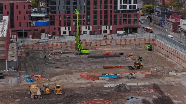 Heavy machinery like a drilling rig and loader operating at a construction site in Canada, workers prepare foundation for new urban building project