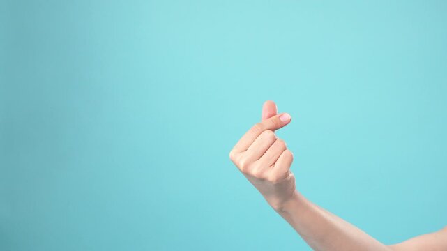 Female hand making Korean finger heart sign on blue background