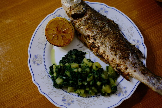 Adriatic sea bass brancin with Dalmatian-style potatoes and spinach stew, roasted lemon half