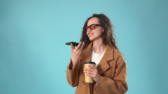 Young woman in brown coat sending voice message on phone