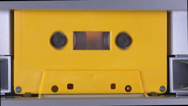 Yellow audio cassette tape playing in a deck
