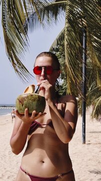 Fit young woman enjoying raw coconut water on tropical beach. Natural hydration, healthy nutrition and refreshing organic drink concept with sunny vacation atmosphere and active lifestyle.