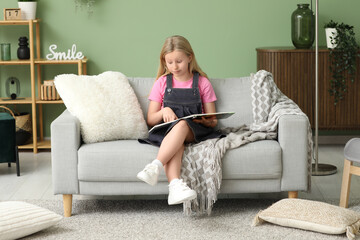 Obraz premium Surprised little girl reading book while sitting on sofa at home