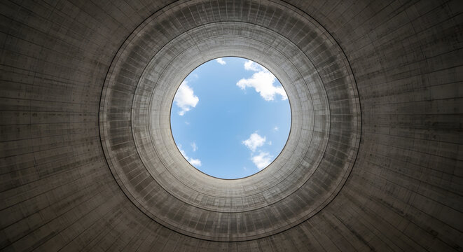 Looking up through a concrete industrial cooling tower at a bright blue sky with white clouds