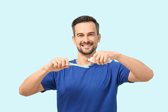 Handsome man squeezing tooth paste onto brush on blue background