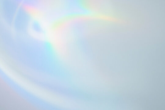 Soft pastel iridescent light leak with subtle rainbow flare on light blue background