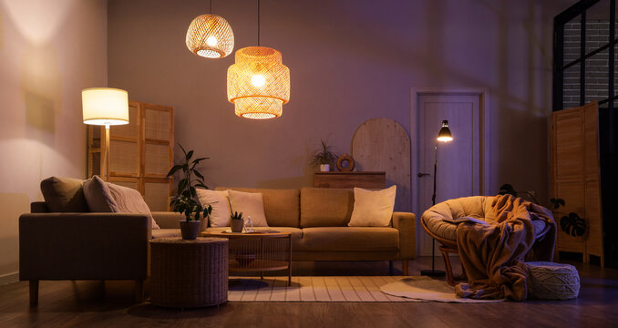 Interior of stylish living room with cozy grey sofas, coffee table and glowing lamps at night