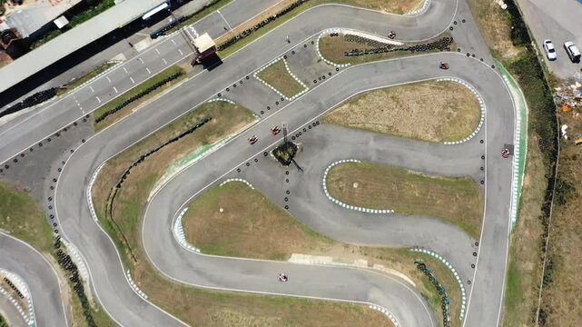 Aerial top view of go kart track with racers moving along winding circuit showing motorsport activity, sharp turns and racing facility