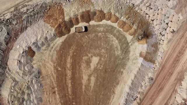 Top down aerial of mine pit with tractors and dump trucks in Utah