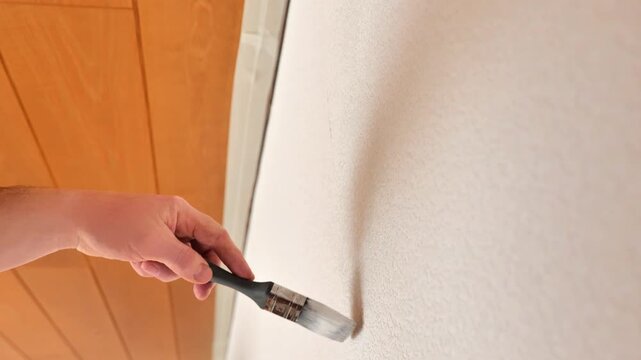 Wall renovation and painting. Movement of a paintbrush in white paint on a textured wall.4k footage