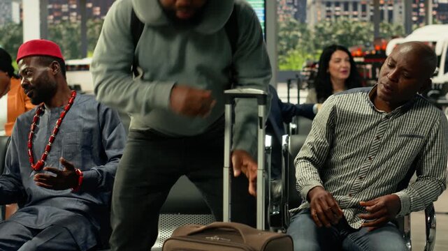 Multiethnic passengers waiting on their long-haul coach in busy bus station, chatting and making friends. People passing time waiting for departure with carry-on trolley bags at bus stop.