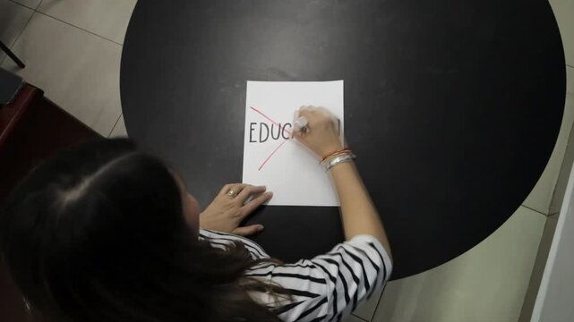Young woman crossing out a sheet of paper with the word education with a red marker on a black table. Horizontal video 