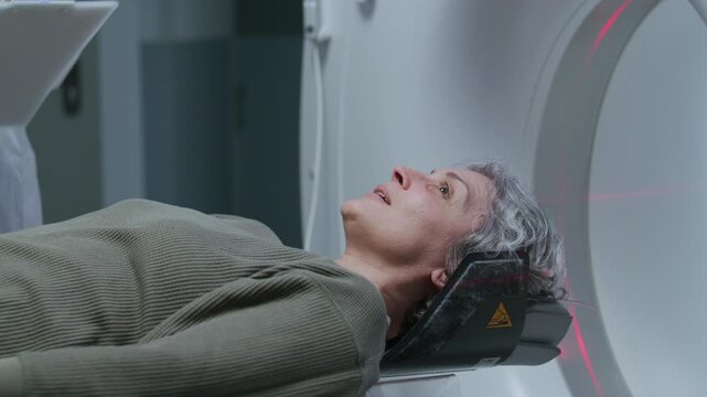Senior female patient sliding out from computed tomography scanner after medical checkup at modern hospital, doctor managing procedure by operating control panel