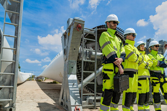 engineers in hard hats and high-visibility jackets inspect a massive piece of industrial equipment on a construction site, collaborating to ensure safety and proper assembly.