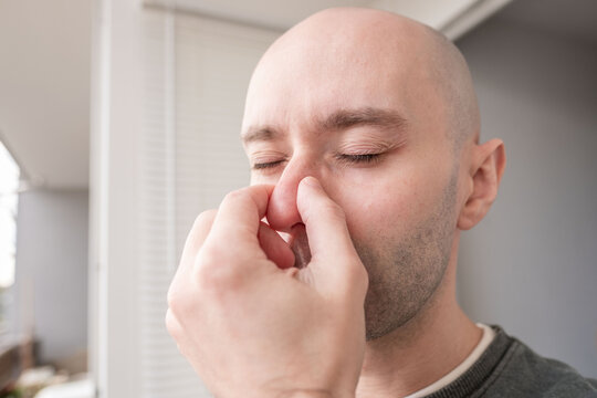 young man touching painful nose with fingers, eyes closed, reacting to unpleasant odor or sinus congestion, reaction unbearable stench, facial expression clearly conveys disgust, physical discomfort