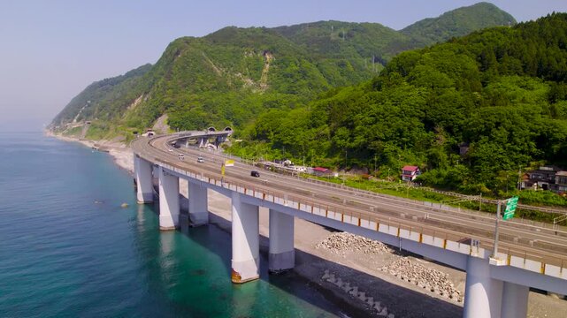 海上から山間部へ続く高速道路 前進しながら右パンでS字カーブを追うドローン空撮